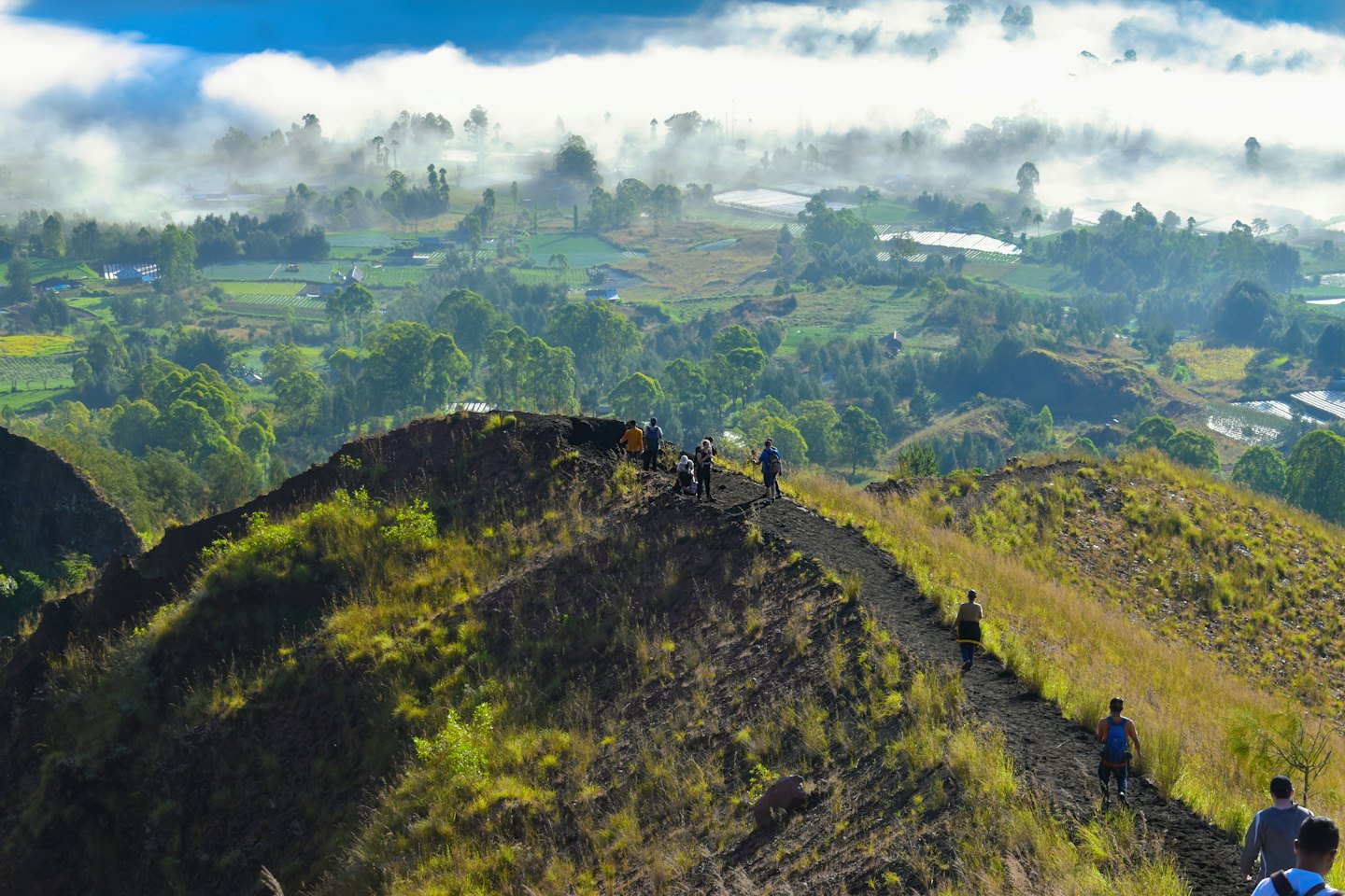 Senderistas suben un camino volcánico con vistas a un valle verde y brumoso.